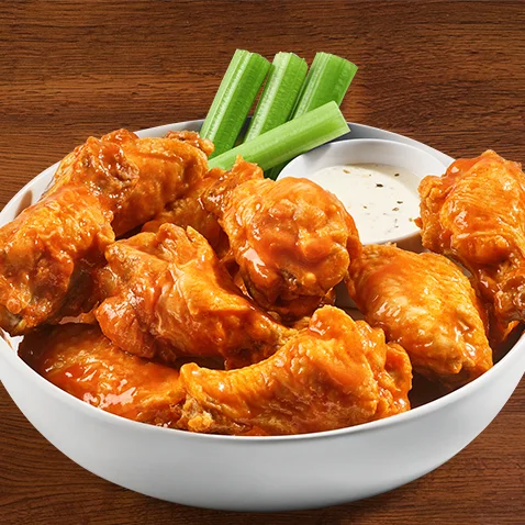 traditional crispy wings tossed in sauce with celery and dipping sauce on the side of the plate